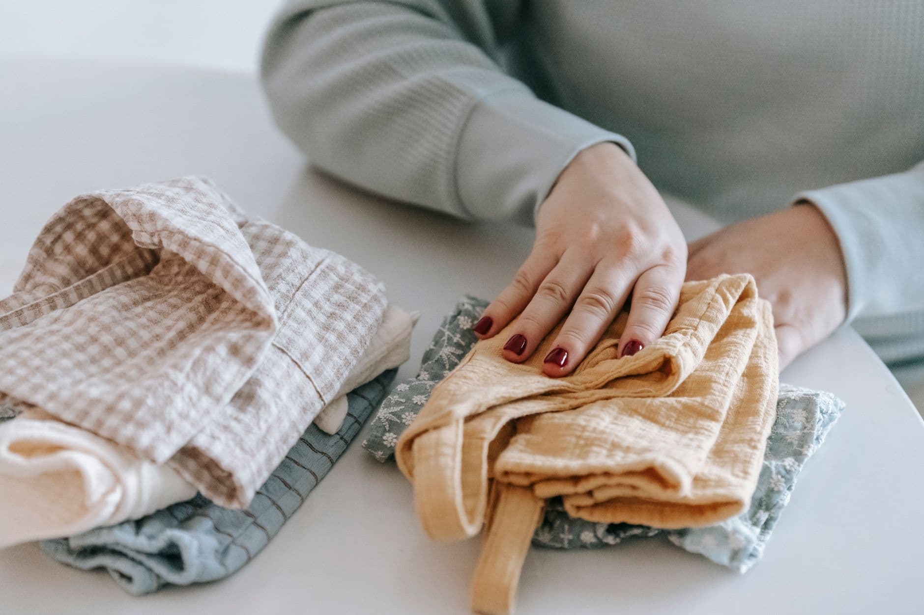 A pair of hands carefully folding colourful baby clothes on a white table