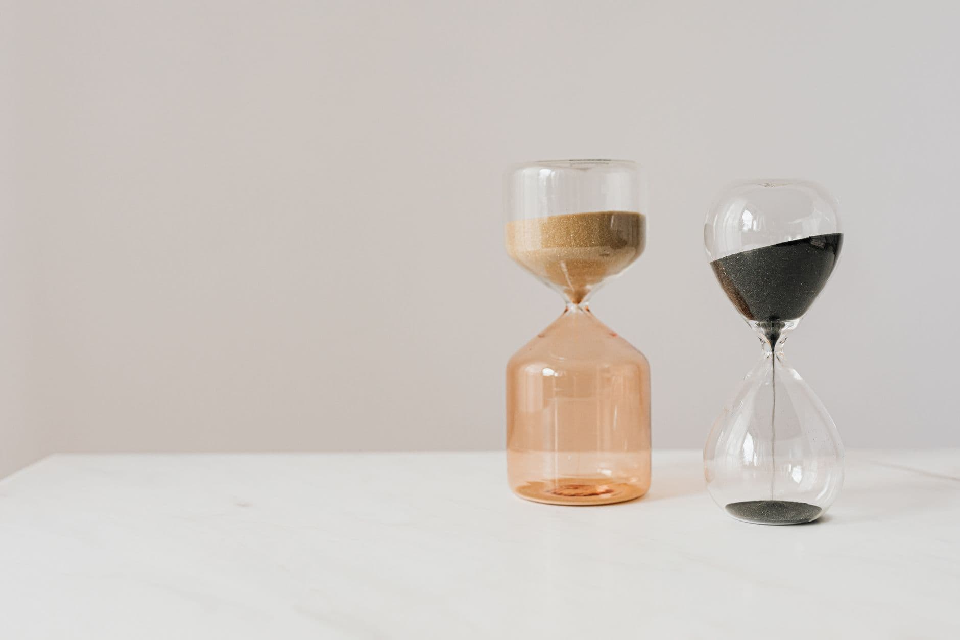 Two hourglasses with beige and black sand on a white surface.