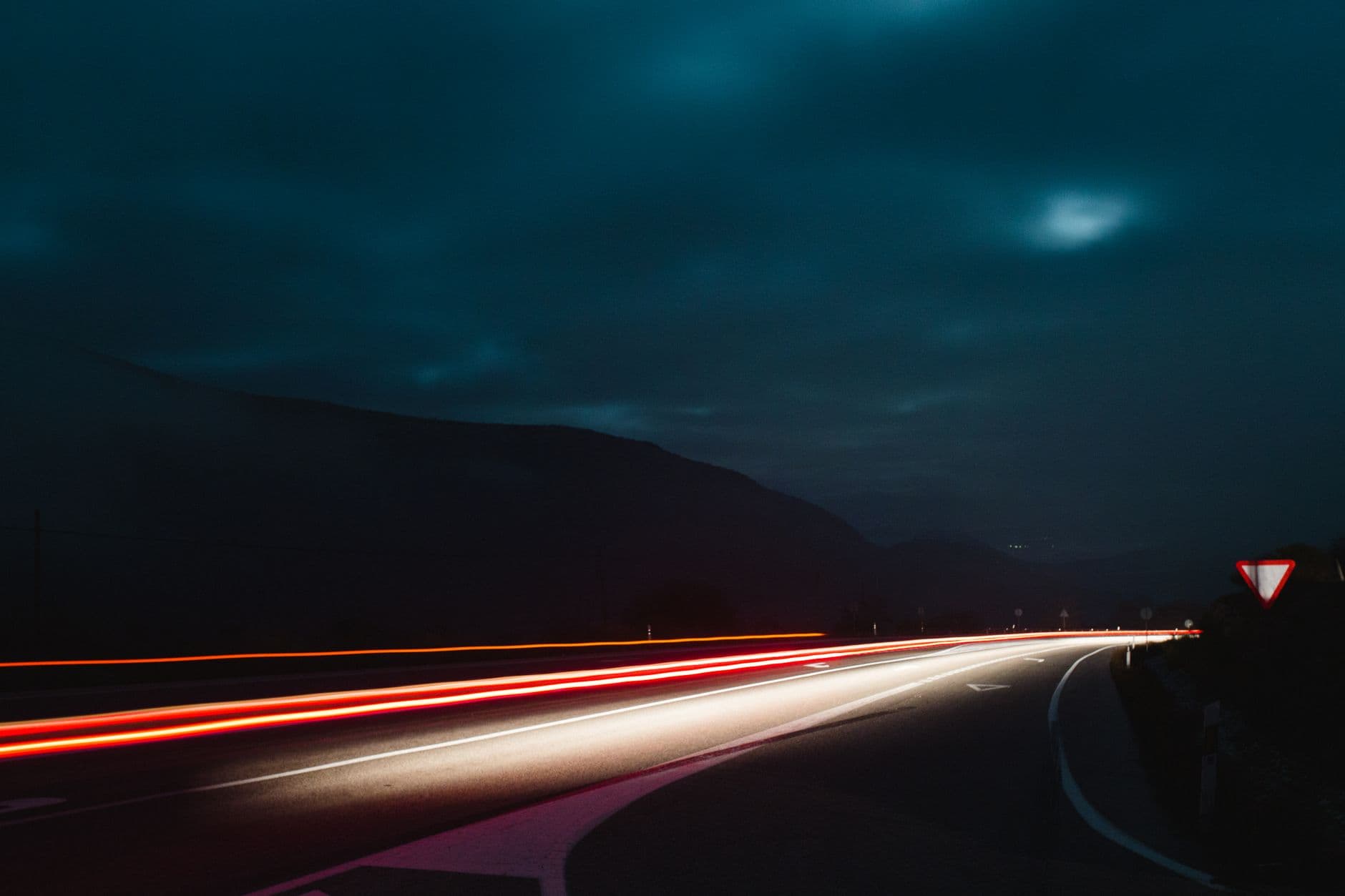A dark curved highway at night with red and white light trails from passing cars.